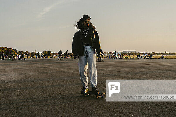 Junge Frau steht auf Skateboard gegen den Himmel im Park