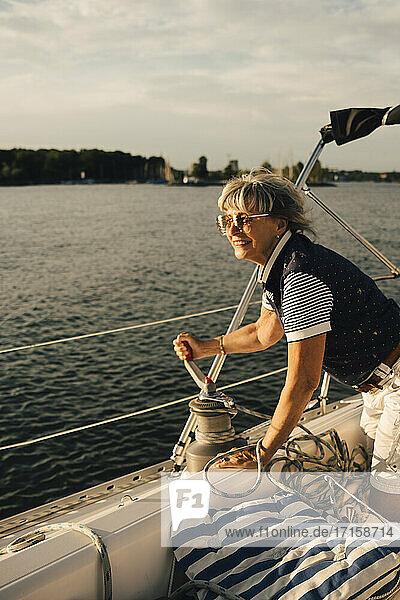 Lächelnde ältere Frau dreht Griff auf Boot im Meer während des sonnigen Tages