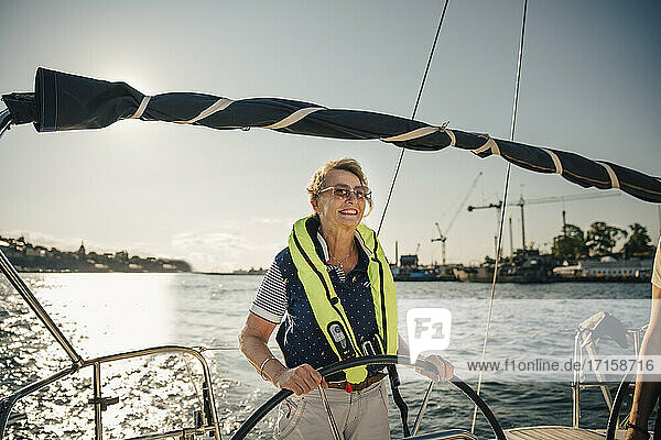 Smiling senior woman sailing boat on sunny day