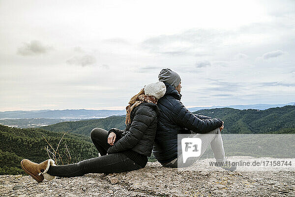 Paar sitzt Rücken an Rücken auf dem Aussichtspunkt gegen den Himmel