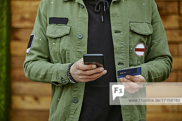 Man in jacket holding smart phone while doing online payment through credit card