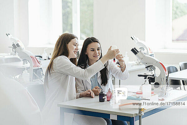 Young female researchers in white coats analyzing laboratory sample in lab