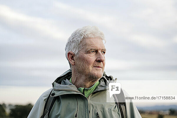 Thoughtful senior male hiker looking away against sky