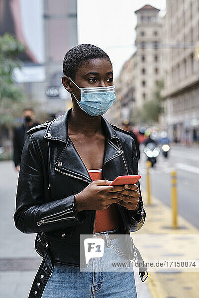 Young woman wearing protective face mask using mobile phone while standing in city