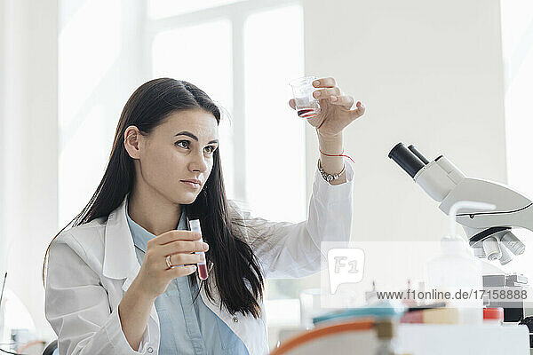 Young female researcher in white coat analyzing laboratory sample