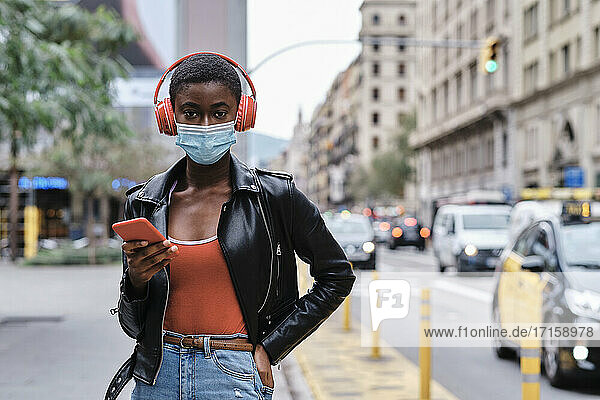 Woman wearing protective face mask and headphones using mobile phone while standing