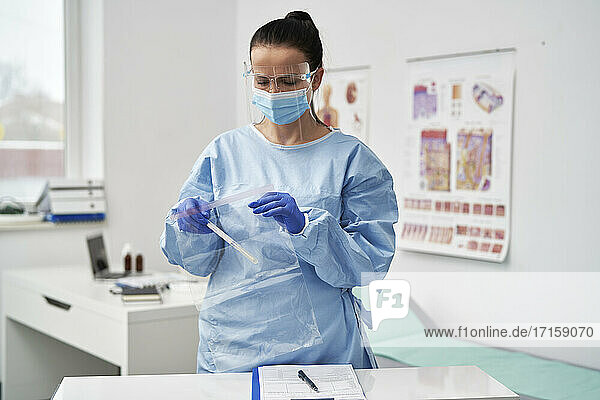 Mature female doctor with face shield putting medical sample in zipper bag