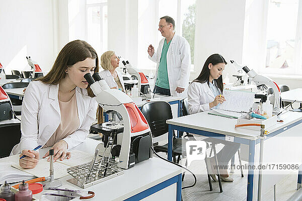 Researcher in white coat working with microscope in science class
