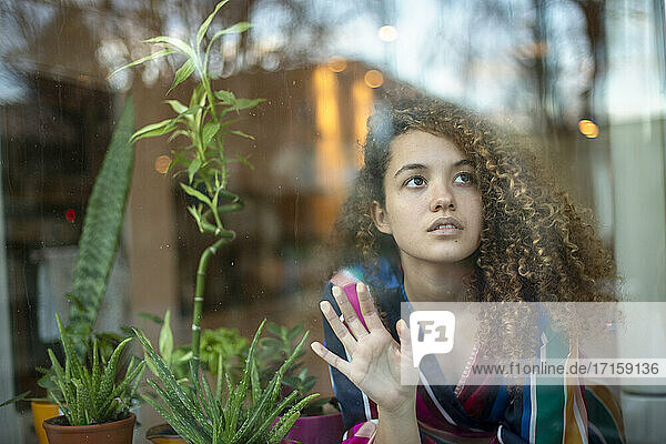 Nachdenkliche junge Frau durch Glasfenster zu Hause gesehen