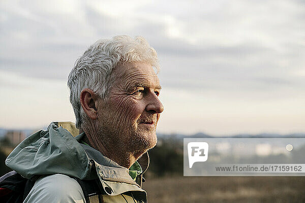 Lächelnder älterer Mann  der bei Sonnenuntergang in die Landschaft blickt