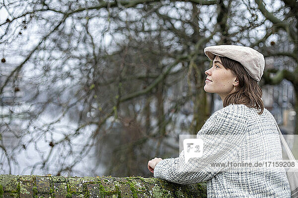Female wearing flat cap standing at retaining wall while looking away