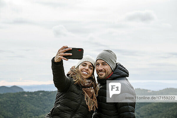 Lächelndes Touristenpaar macht ein Selfie gegen den Himmel im Winter