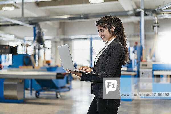 Young entrepreneur using laptop while standing at industry