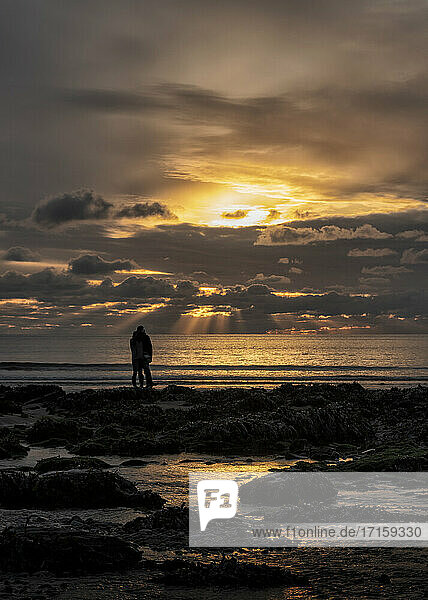 Silhouette eines Paares  das am Strand von Manorbier  Pembrokeshire  Großbritannien  steht und die Aussicht betrachtet