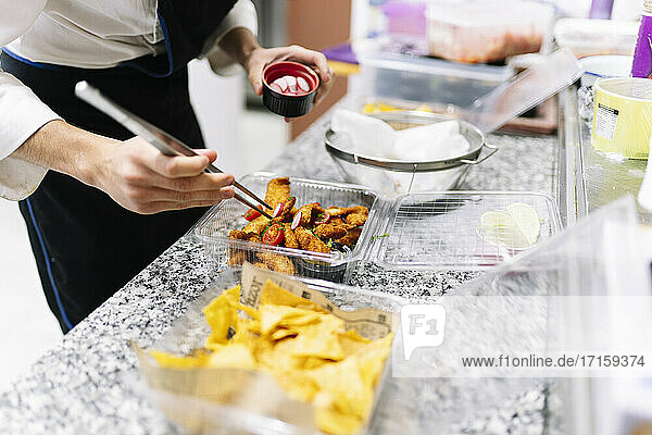 Männlicher Koch  der Essen in Plastikbehältern auf dem Küchentresen eines Restaurants garniert