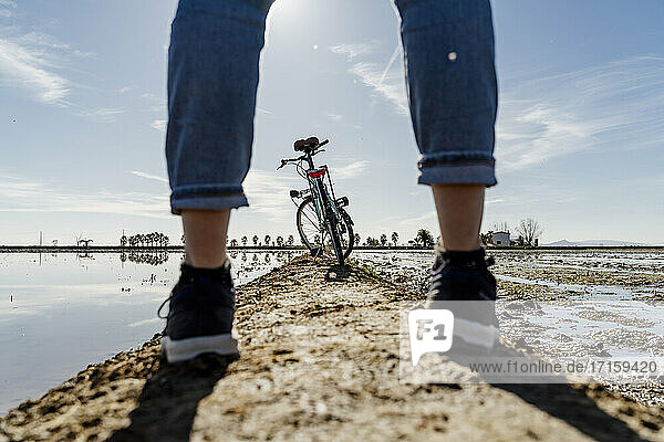 Fahrrad durch die Beine einer Frau auf dem Fußweg im Ebro-Delta an einem sonnigen Tag  Spanien