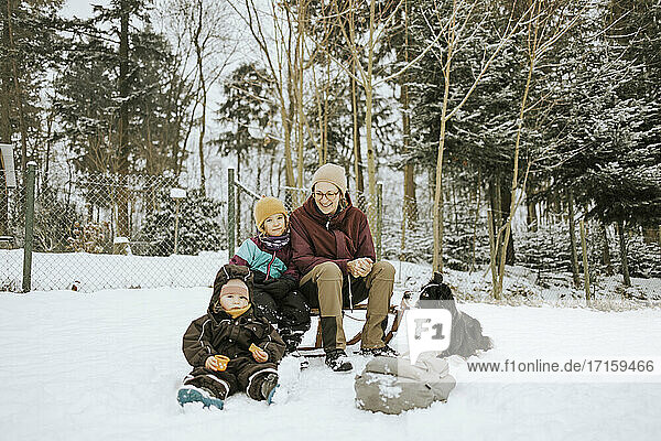 Mother with daughters and Border Collie sitting on snow covered field against trees