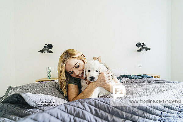 Woman embracing Golden Retriever puppy while lying on bed at home