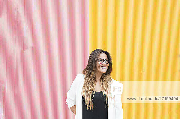 Smiling young woman standing against pink and yellow wall