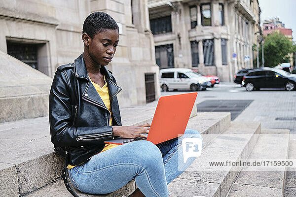 Young woman working on laptop while sitting in city
