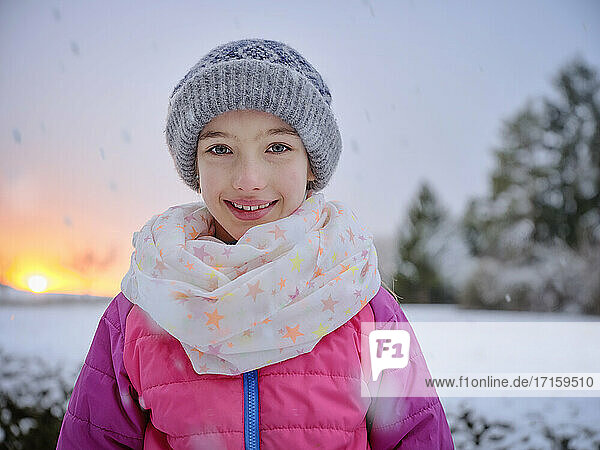 Cute smiling girl in warm clothing during sunset in winter