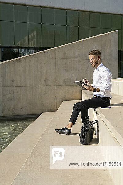 Mid adult businessman using digital tablet while sitting on steps