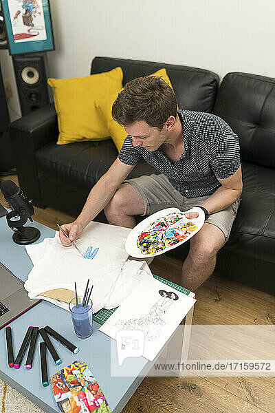 Male artist painting in paper while sitting at home