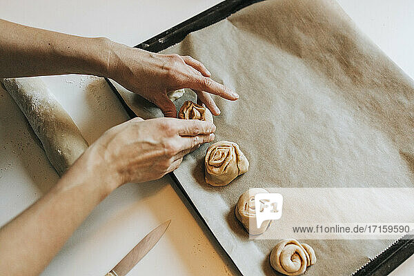 Woman arranging cinnamon rolls on baking sheet