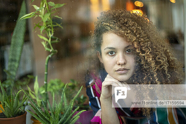 Junge Frau mit Hand am Kinn  die durch ein Glas zu Hause schaut