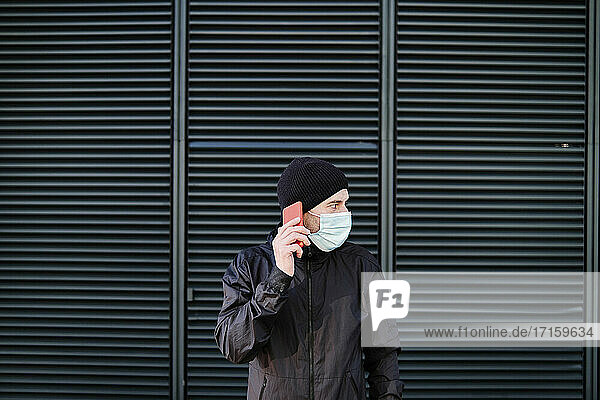 Man in protective face mask talking on the phone against shutter