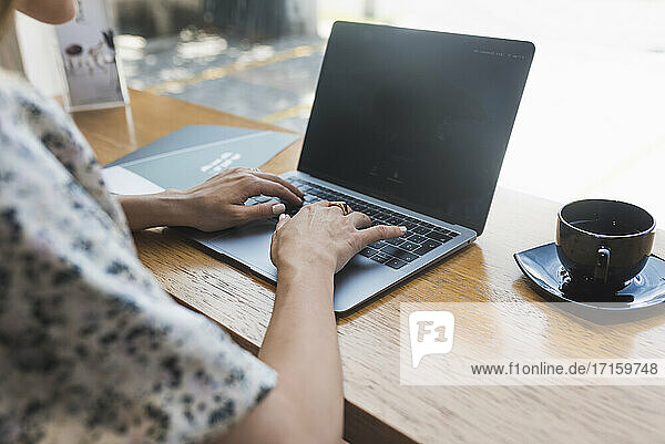Hands of businesswoman working over laptop by coffee shop in cafe
