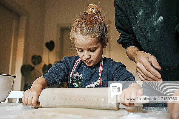 Mädchen hilft ihrer Mutter in der Küche beim Ausrollen von Teig für Zimtschnecken