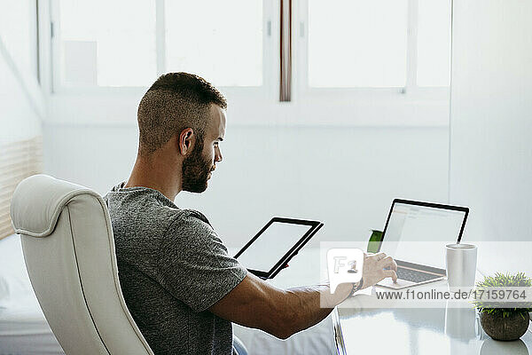 Junger Mann arbeitet zu Hause an Laptop und Tablet