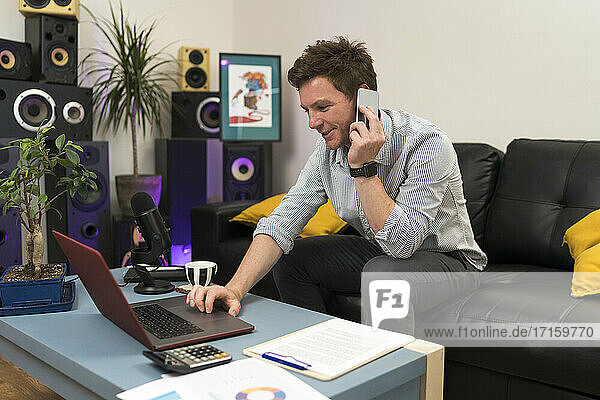 Unternehmer  der mit dem Handy telefoniert  während er im Büro zu Hause einen Laptop benutzt