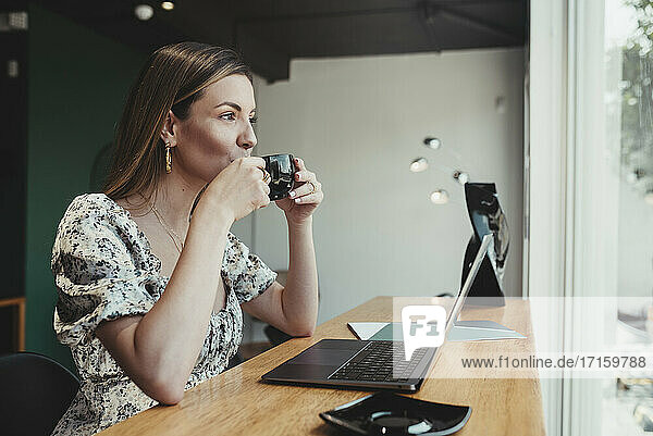 Geschäftsfrau mit Laptop auf dem Tisch  die Kaffee trinkt  während sie in einem Café sitzt