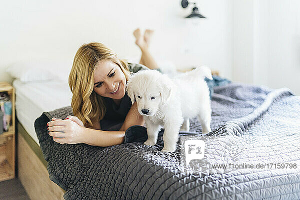 Smiling woman looking at Golden Retriever puppy while lying on bed