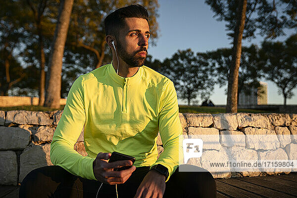Male athlete listening music at park during sunset