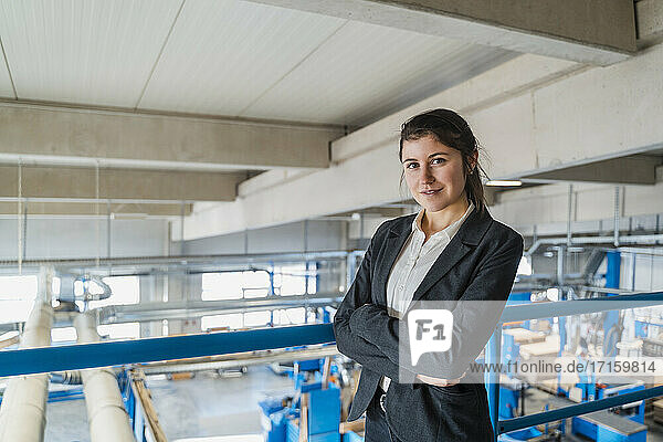 Smiling businesswoman with arms crossed standing by railing at industry