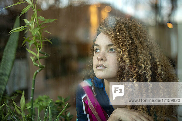 Nachdenkliche junge Frau schaut durch das Fenster
