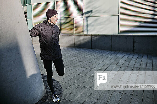 Male runner doing stretching exercise by wall during sunny day