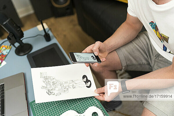 Künstler  der zu Hause sitzend mit seinem Handy ein Designfoto aufnimmt