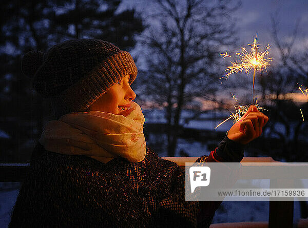 Playful girl in warm clothing holding sparkler during winter