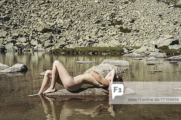 Naked woman sunbathing while lying on rock in lake during sunny day