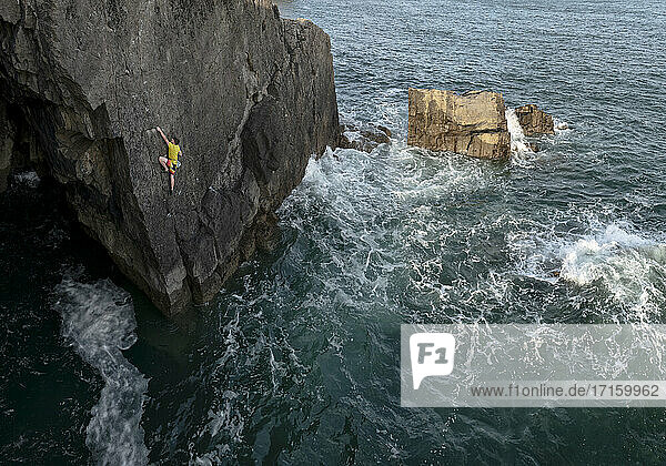 Junger männlicher Felskletterer klettert auf Felsen gegen das Meer
