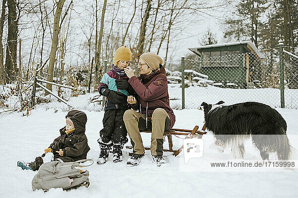 Mutter  die ihre Tochter füttert  während sie im Winter im Schnee ein Wochenende mit der Familie verbringt