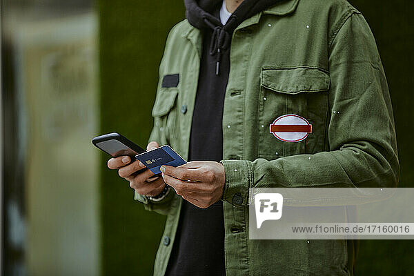 Man in jacket holding mobile phone while doing online shopping through credit card