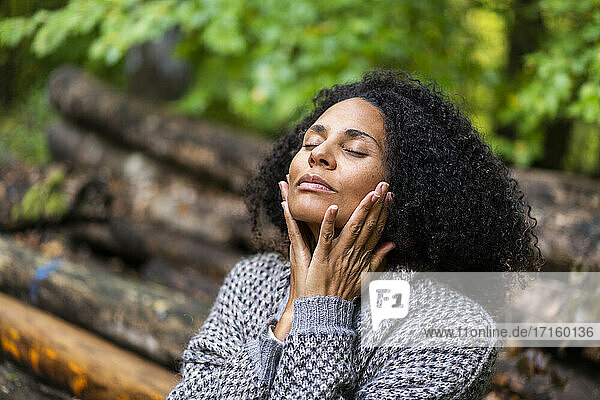 Lockenköpfige Frau sitzt mit geschlossenen Augen im Wald