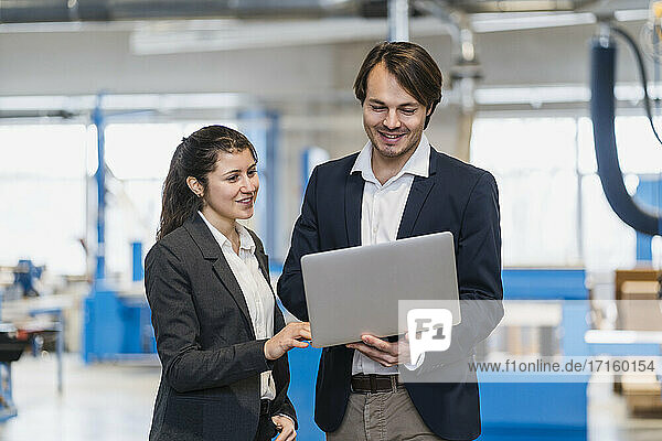 Smiling expertise working on laptop while standing at industry