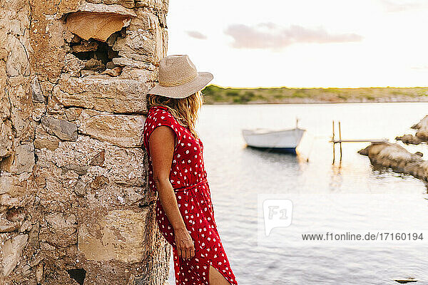Frau mit Hut schaut auf die Aussicht und lehnt sich an eine Mauer am See