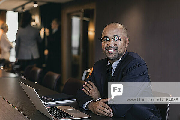 Porträt von lächelnden kahlen Geschäftsmann sitzt mit Laptop am Konferenztisch im Sitzungssaal